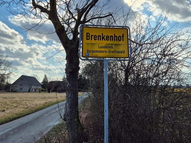 Ortseingangsschild Brenkenhof an einer Dorfstraße.