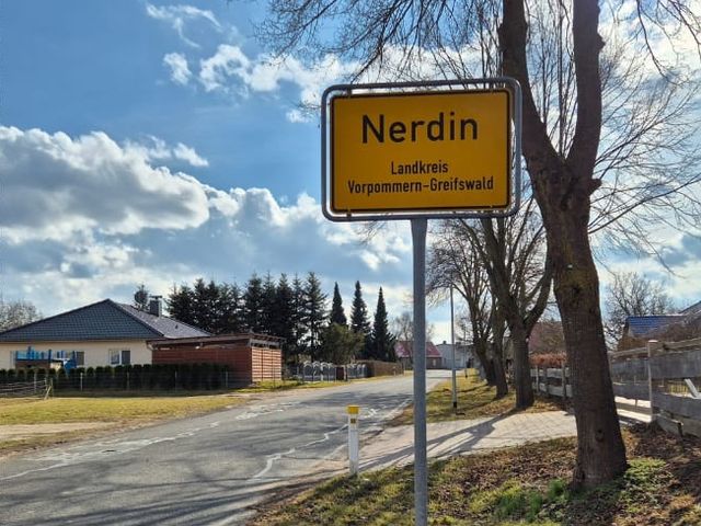 Ortseingangsschild Nerdin, dahinter Häuser und Bäume.