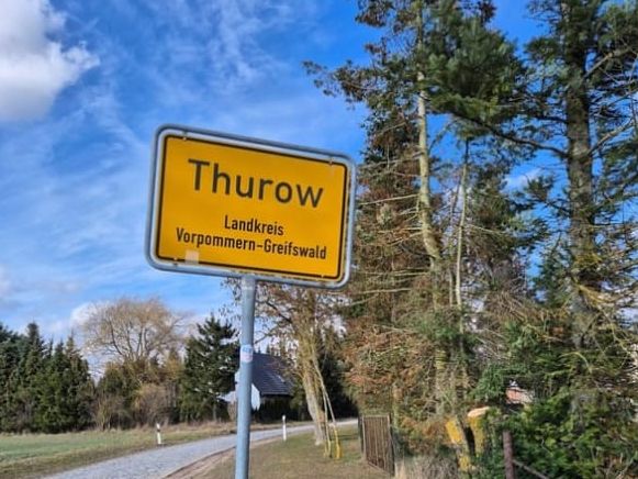 Ortseingangsschild Thurow am Rand einer Allee.